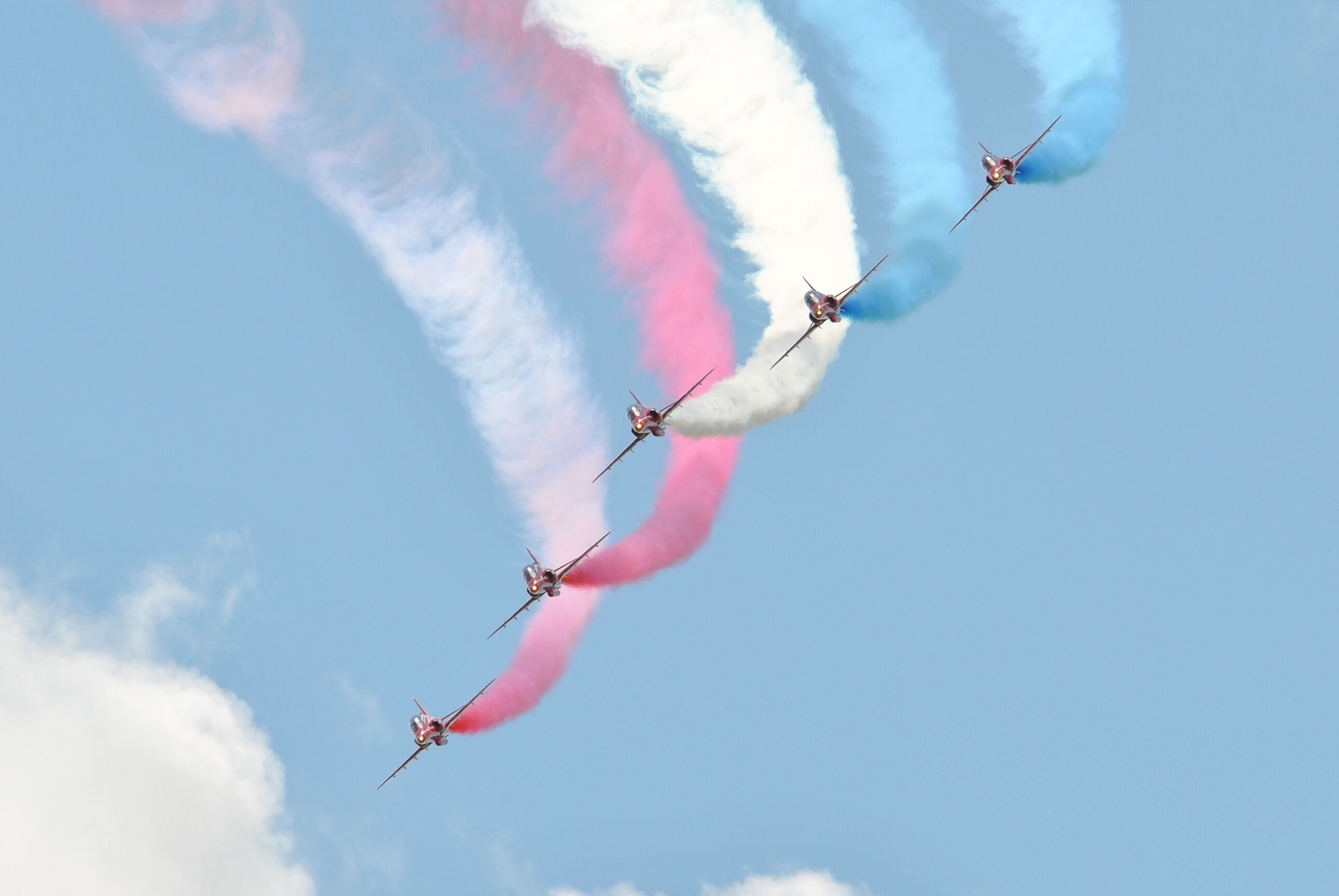 Four jets flying in formation with pink, white, and blue smoke trails.