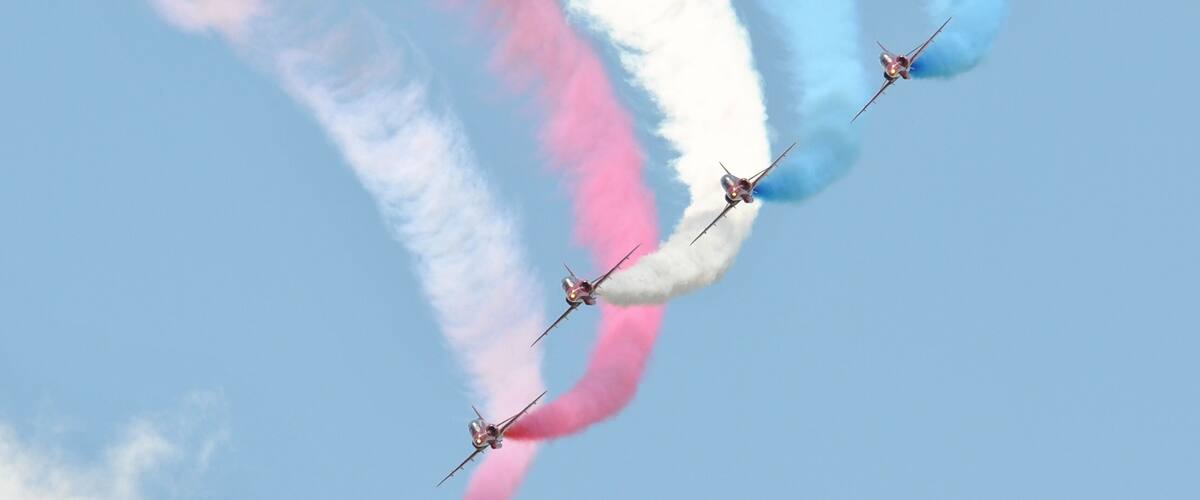 Four jets flying in formation with pink, white, and blue smoke trails.