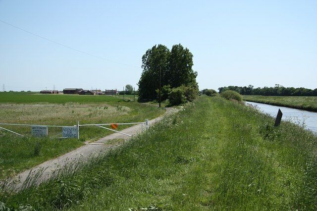 A grassy path beside a canal with a fence and signs.