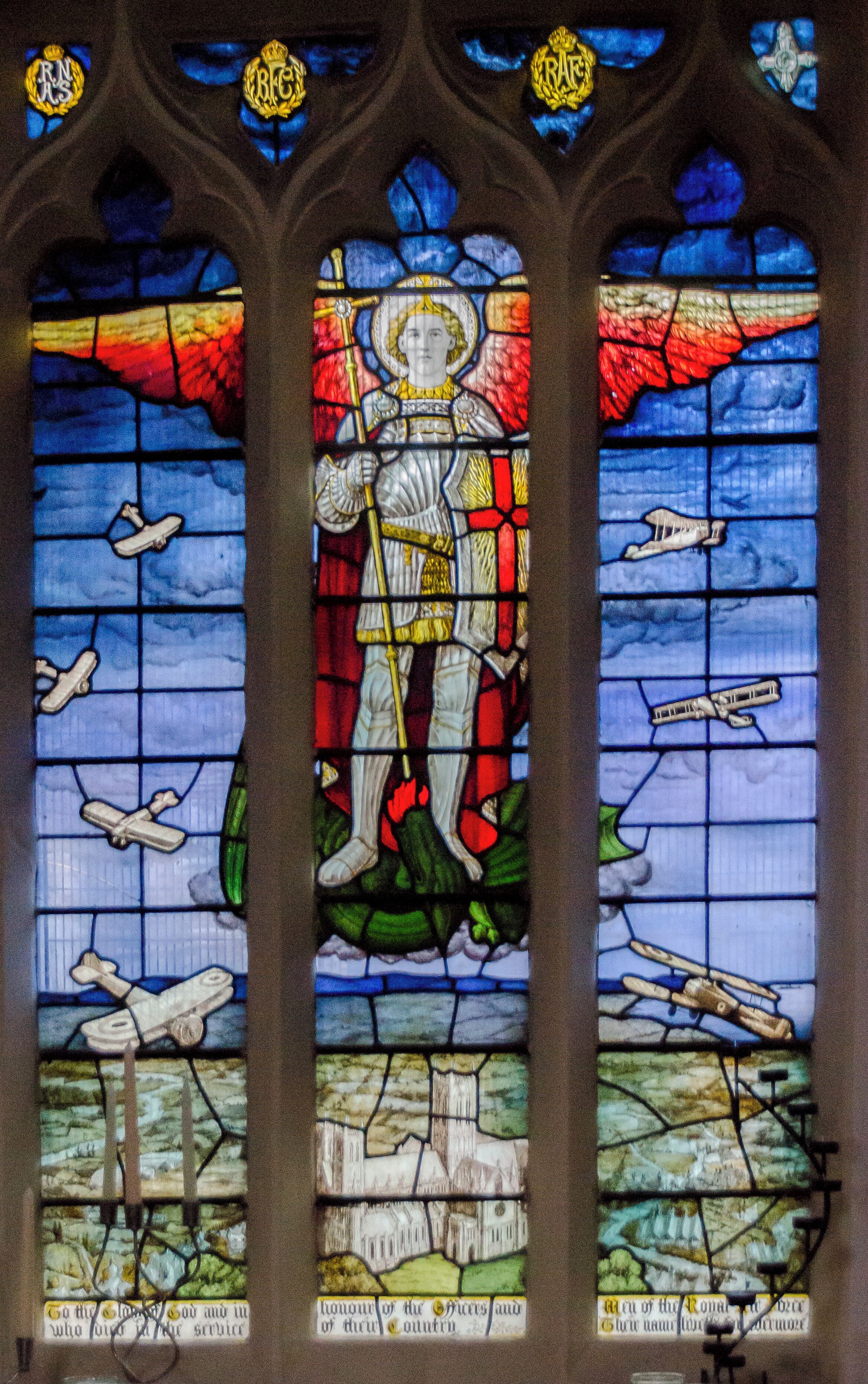 The background for this window consists of clouds coloured in airforce blue and the view of Lincoln Cathedral is seen from the air and was taken from a photograph provided by the RAF. The window comprises of 3 lights:- The centre light portrays St Michael the Archangel, fully armed, as patron of the Church Militant, piercing the Dragon of Evil, standing sentinel over the Cathedral of Lincoln. The Right Side Light shows various types of aeroplanes ascending, such as were flown by pilots at that time. These include the Sopwith Camel, Blackburn Bombers and Avros. There is also a distant view of an early submarine on the surface of the sea. The left hand light contains views of aeroplanes descending to their Hangers in the left foreground. At the top of the Lights can be seen four smaller lights. These feature the badges of the Royal Flying Corps, The Royal Naval Air Service, The Royal Air Force together with The Royal Flying Cross. The window was designed by Messrs Burlison & Grylls of 36, Great Ormond Street, London, WC1, from suggestions made by the Rev Alfred Hunt MA, Vicar of Welton, and was first unveiled and dedicated by the Lord Bishop of Lincoln on 10th May 1921. This unique Memorial Window created considerable interest nationally and among the first to visit was Sir William Tritton the inventor of the Modern Tank. (From Church Guide Book)