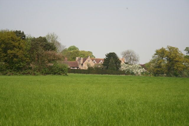 A green field with a house and trees in the background.