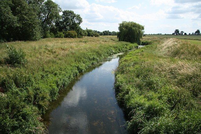 A narrow water channel flanked by grassy banks and trees.