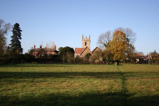 A church with a tall tower, surrounded by houses and a grassy field.