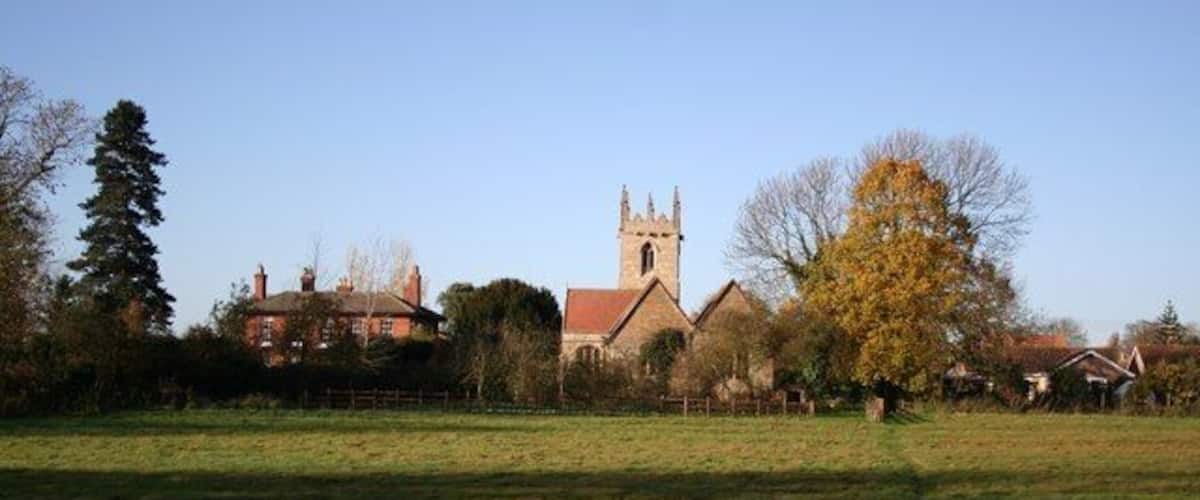 A church with a tall tower, surrounded by houses and a grassy field.
