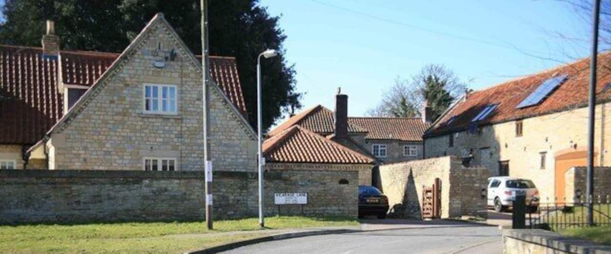 A quiet residential street with stone houses, a parked car, and a clear sky.