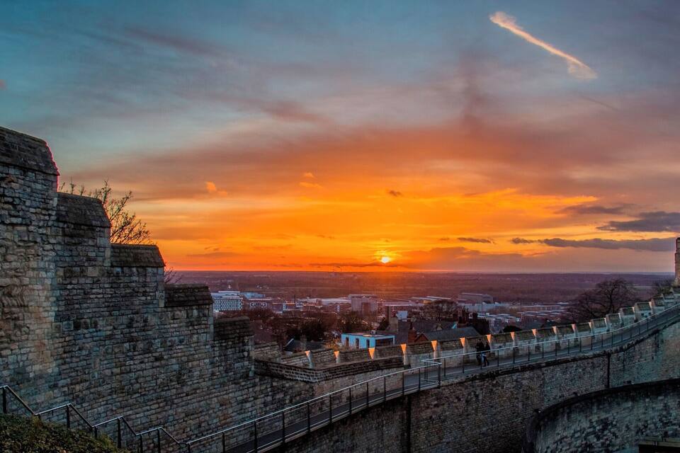 Un coucher de soleil sur une ville, avec un mur de pierre et un pont.