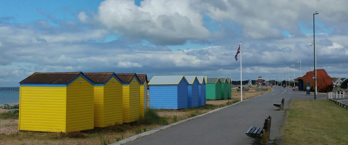 A coastal road with colorful beach huts and a flagpole.