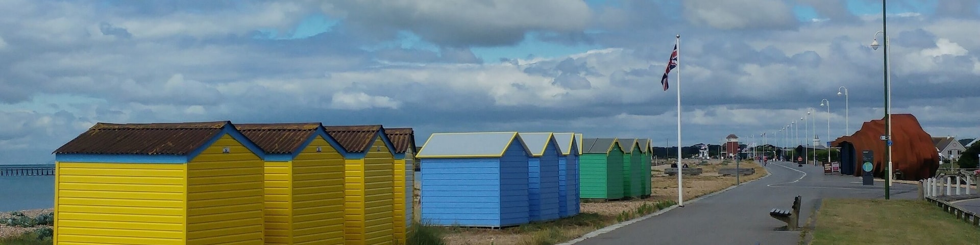 A coastal road with colorful beach huts and a flagpole.