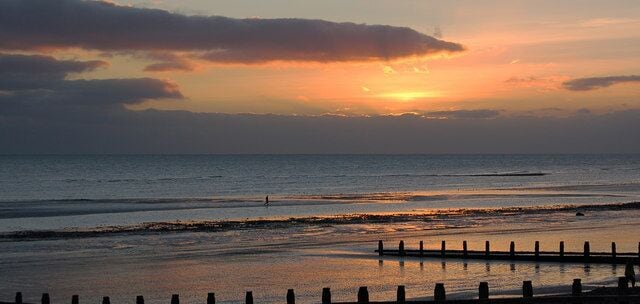A beach at sunset with calm waters and a wooden fence in the foreground.