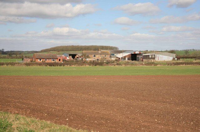 A rural landscape with a farm, open fields, and a distant hill.
