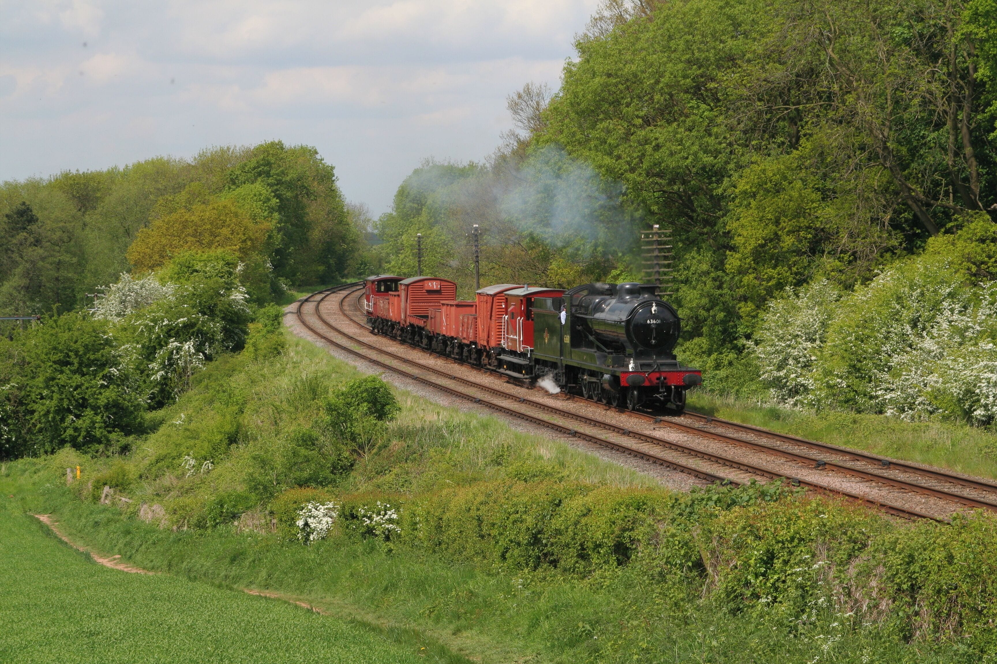 A steam locomotive pulling red freight cars on a curved railway track through a lush green landscape.