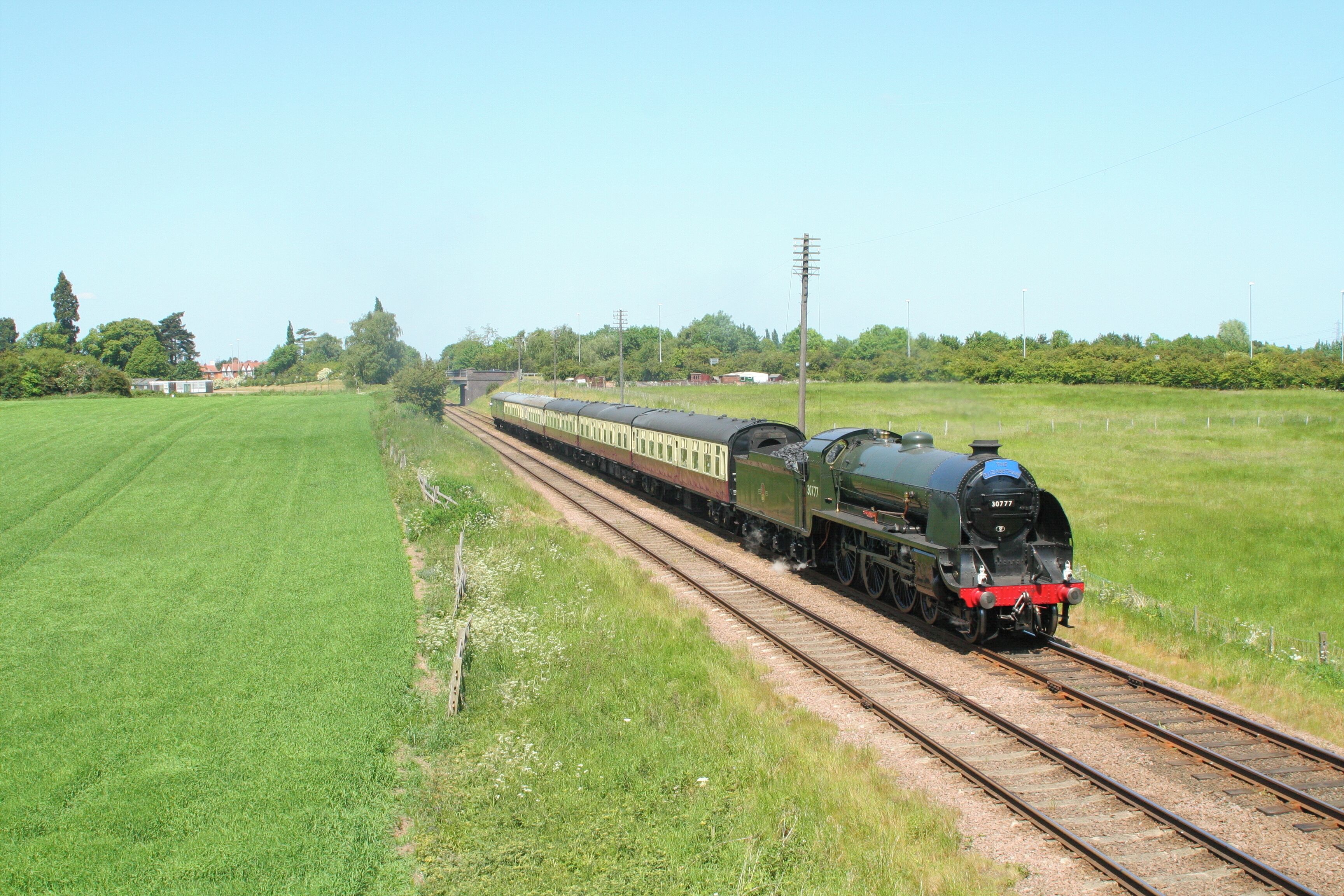 A green steam locomotive pulling passenger cars on a rural railway track.