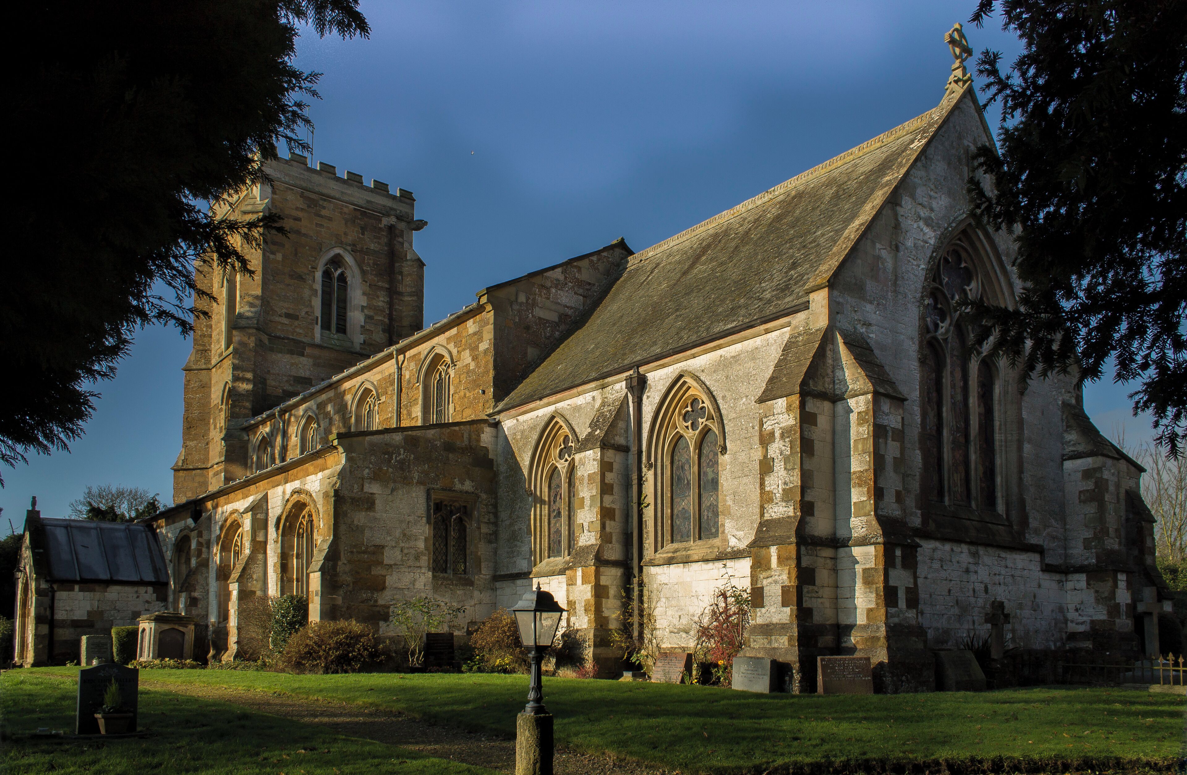 The church dates from the 13th century onwards. The nave was rebuilt in 1843, and the chancel in 1873 by Fowler. The church is built from ironstone with limestone dressings, with a slate and lead roof. There is a western tower with three bells, nave with clerestory, north and south aisles, chancel and south porch. The church originally consisted of tower, nave, chancel and south aisle only, and there is no record of any restoration before 1831. The four bay south arcade is early 13th century with circular piers. The north arcade is all 19th century. The nave roof is 19th century, but incorporates 15th C. carved wooden figures to the hammer beams. The ceiling has been elaborately decorated with roundels containing paintings of Saints. The words of the Te Deum are written around the walls of the chancel at the border with the roof, and the theme of the decoration relates to the first verse of the Te Deum. There is a fine sculptured stone reredos, painted and gilded. The organ is also painted and gilded by J.G. Smyth. All fittings are 19th century apart from the 15th century octagonal font. The 2 manual organ is by Nicholson of Worcester from 1904. Photo by J.Hannan-Briggs