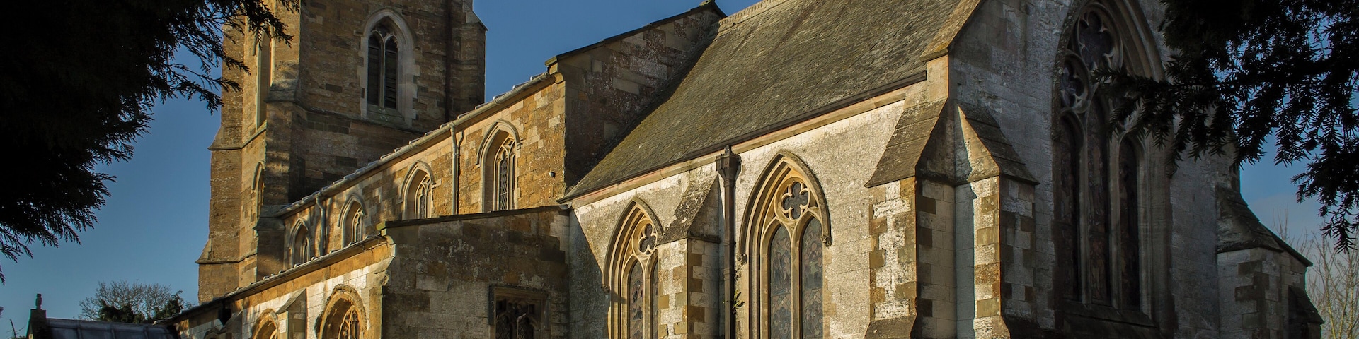 The church dates from the 13th century onwards. The nave was rebuilt in 1843, and the chancel in 1873 by Fowler. The church is built from ironstone with limestone dressings, with a slate and lead roof. There is a western tower with three bells, nave with clerestory, north and south aisles, chancel and south porch. The church originally consisted of tower, nave, chancel and south aisle only, and there is no record of any restoration before 1831. The four bay south arcade is early 13th century with circular piers. The north arcade is all 19th century. The nave roof is 19th century, but incorporates 15th C. carved wooden figures to the hammer beams. The ceiling has been elaborately decorated with roundels containing paintings of Saints. The words of the Te Deum are written around the walls of the chancel at the border with the roof, and the theme of the decoration relates to the first verse of the Te Deum. There is a fine sculptured stone reredos, painted and gilded. The organ is also painted and gilded by J.G. Smyth. All fittings are 19th century apart from the 15th century octagonal font. The 2 manual organ is by Nicholson of Worcester from 1904. Photo by J.Hannan-Briggs