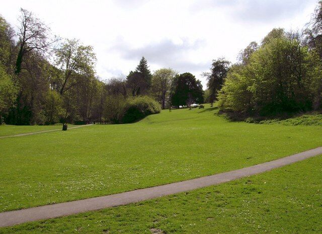 Um parque com um campo gramado, um caminho para pedestres e árvores.