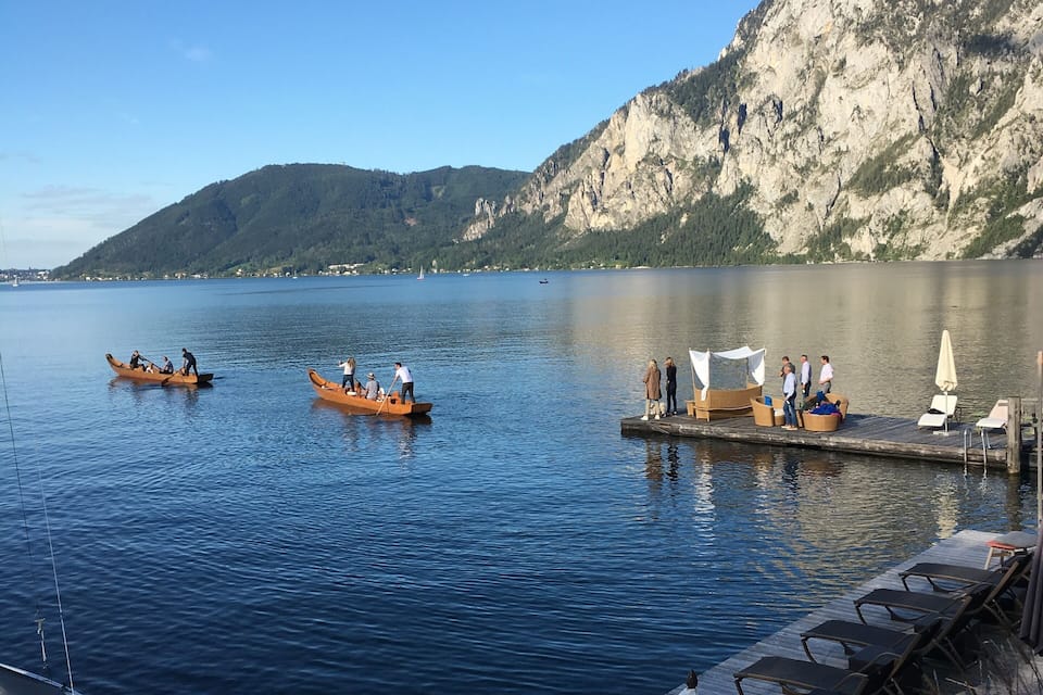 A calm lake with boats, a wooden dock, and a mountain in the background.