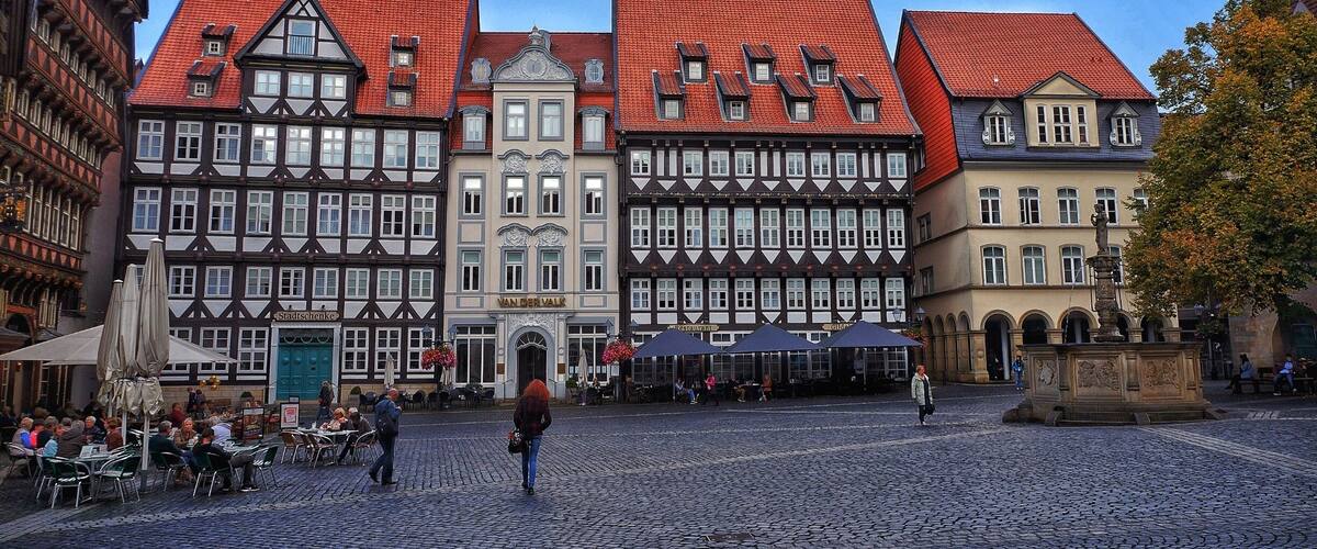 A cobblestone square with historic buildings, a fountain, and outdoor seating.