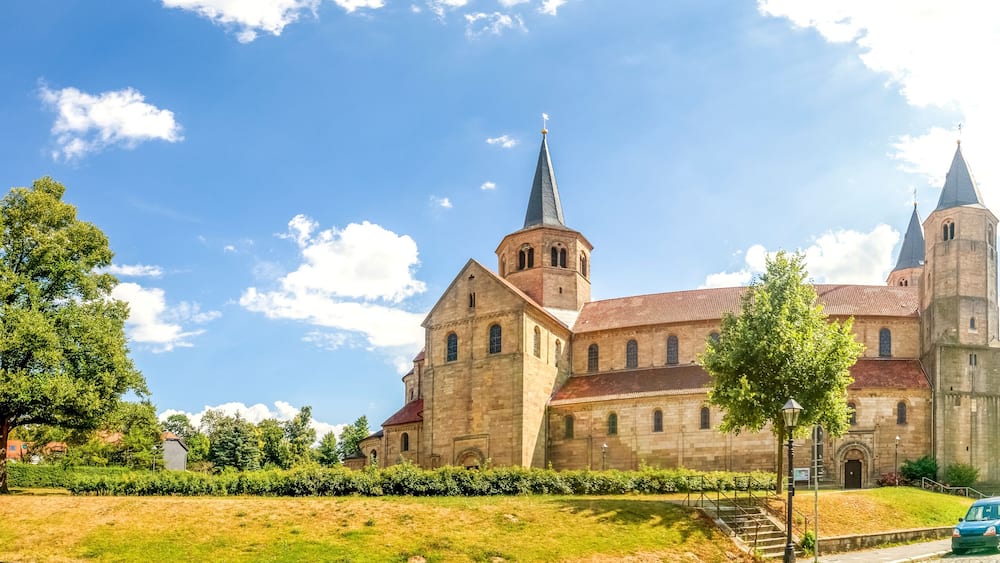 Eine historische Kirche mit einem hohen Kirchturm und einem Glockenturm, umgeben von Bäumen und einem Kopfsteinpflasterweg.