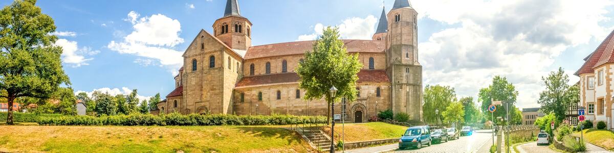 Eine historische Kirche mit einem hohen Kirchturm und einem Glockenturm, umgeben von Bäumen und einem Kopfsteinpflasterweg.