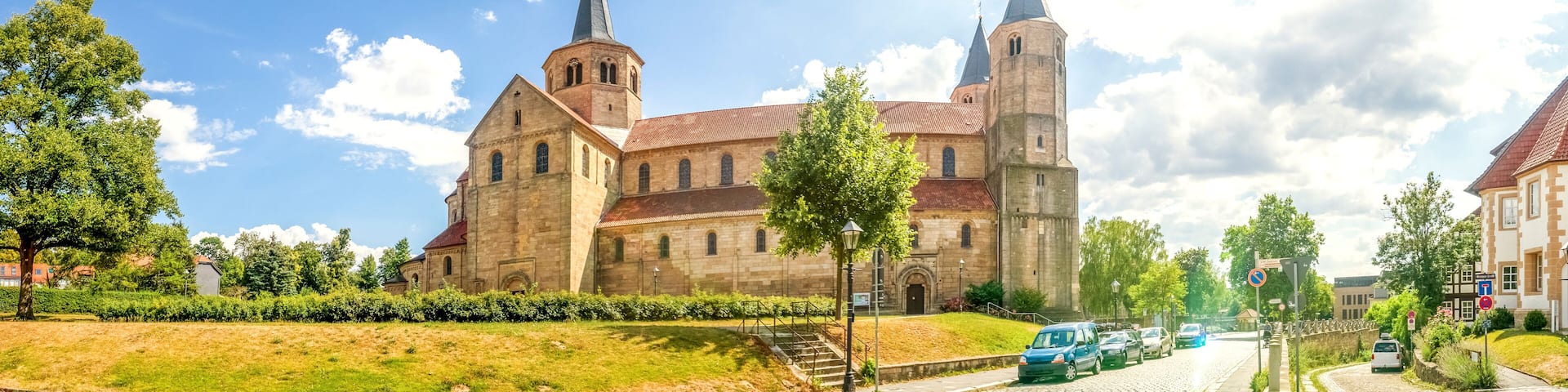 A historic church with a tall spire and a clock tower, surrounded by trees and a cobblestone street.