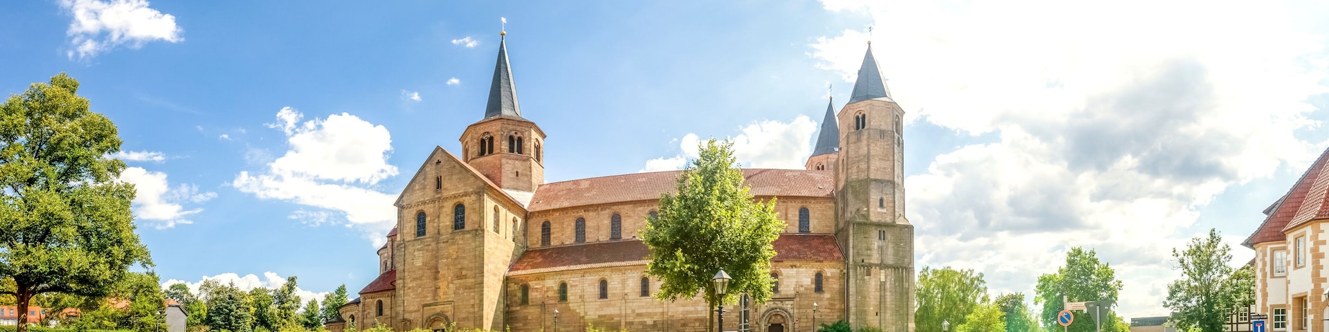 Una iglesia histórica con una aguja alta y un campanario, rodeada de árboles y una calle empedrada.