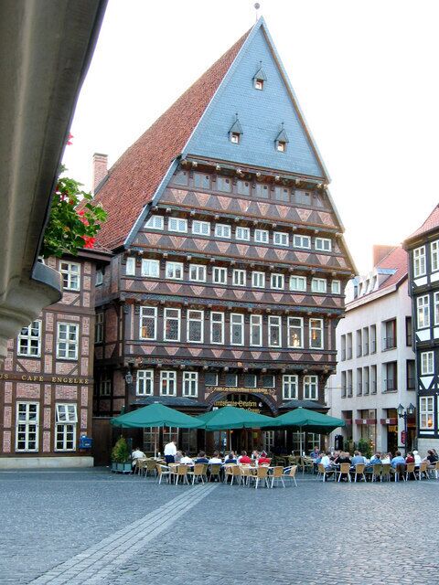 A traditional half-timbered building with a steeply pitched roof and a café with outdoor seating in front.