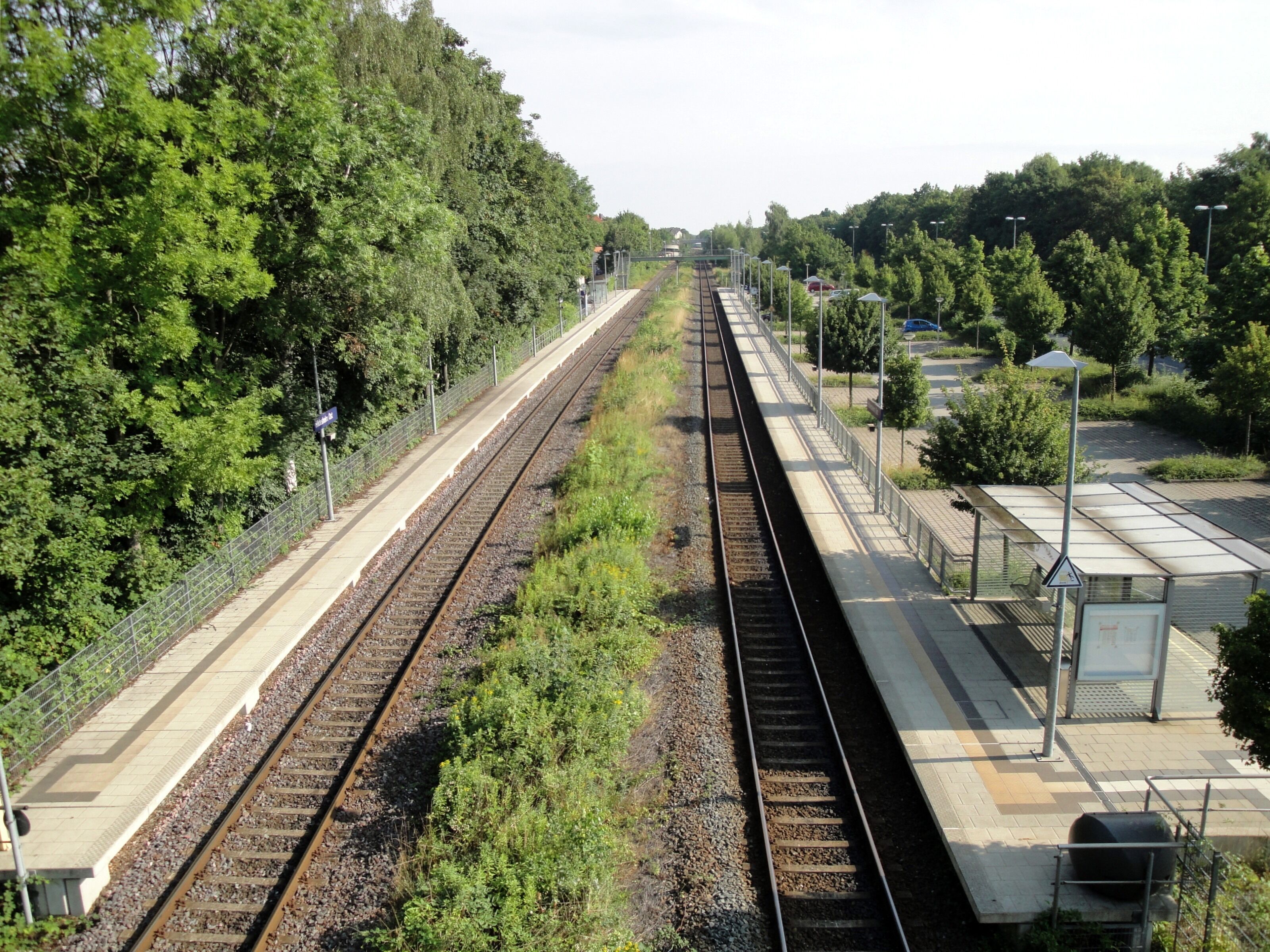 A railway station with multiple tracks, surrounded by lush greenery and trees.