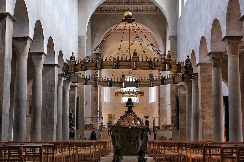 An interior of a cathedral with high ceilings, arched columns, and a large chandelier.