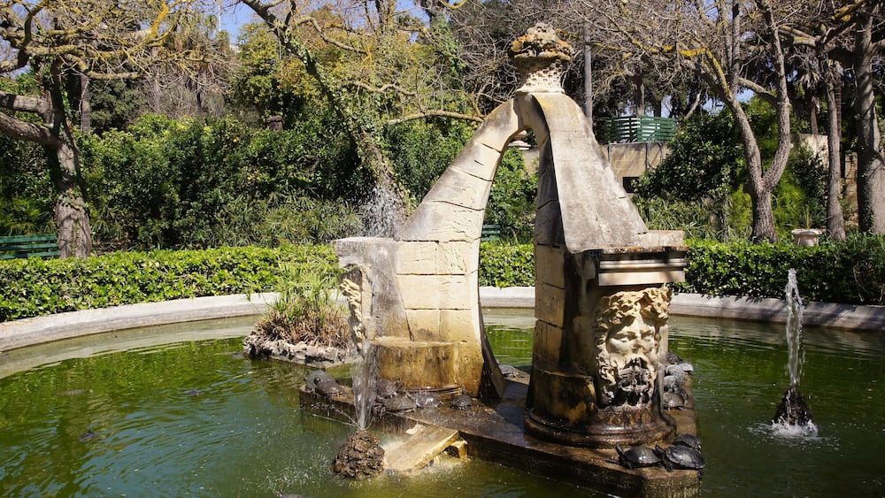 Une fontaine en pierre, avec des jets d’eau et une statue, dans un parc.