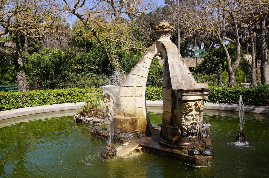 A stone fountain with water spouts and a statue in a park.