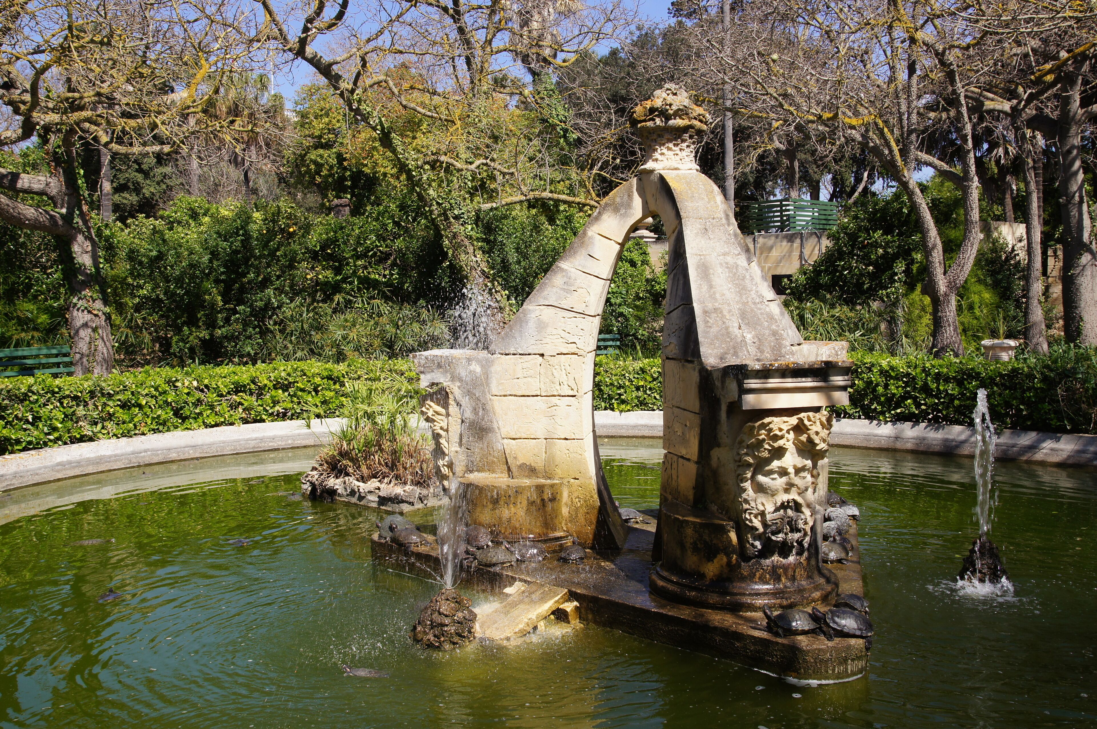 A stone fountain with water spouts and a statue in a park.