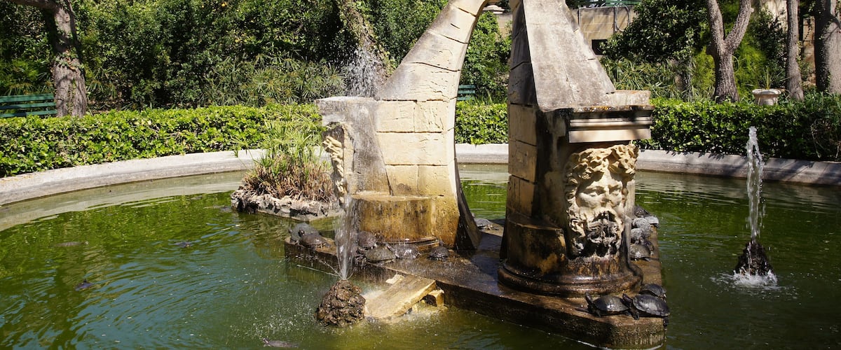 A stone fountain with water spouts and a statue in a park.
