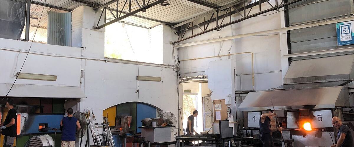 A glass factory with workers operating furnaces and handling glass pieces.
