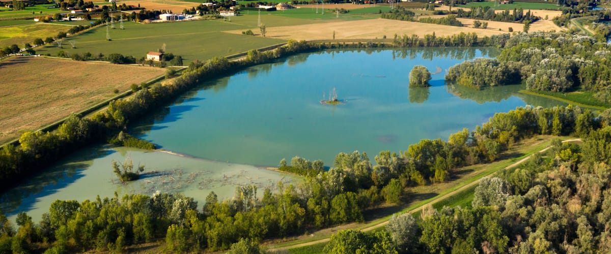 An aerial view of a lake surrounded by dense forests and agricultural fields.