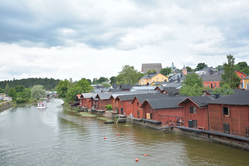 A river with boats, red wooden houses, and a large yellow building in the background.