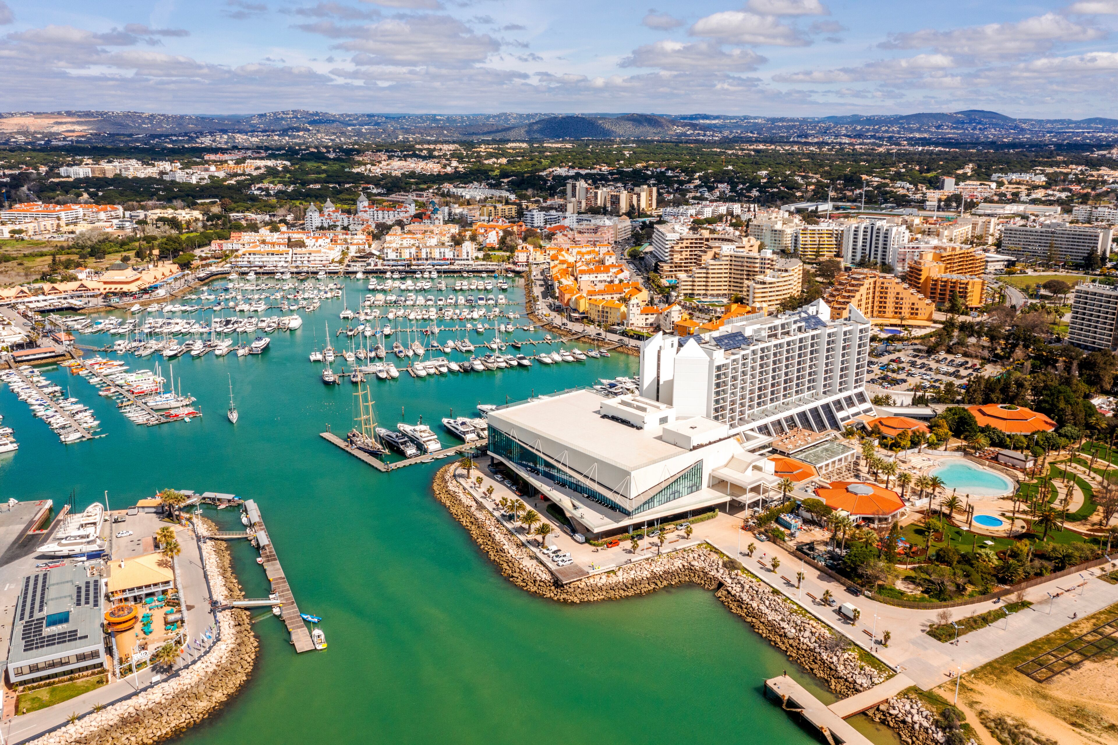 Una marina con numerosos barcos, un gran hotel y un paisaje urbano costero.