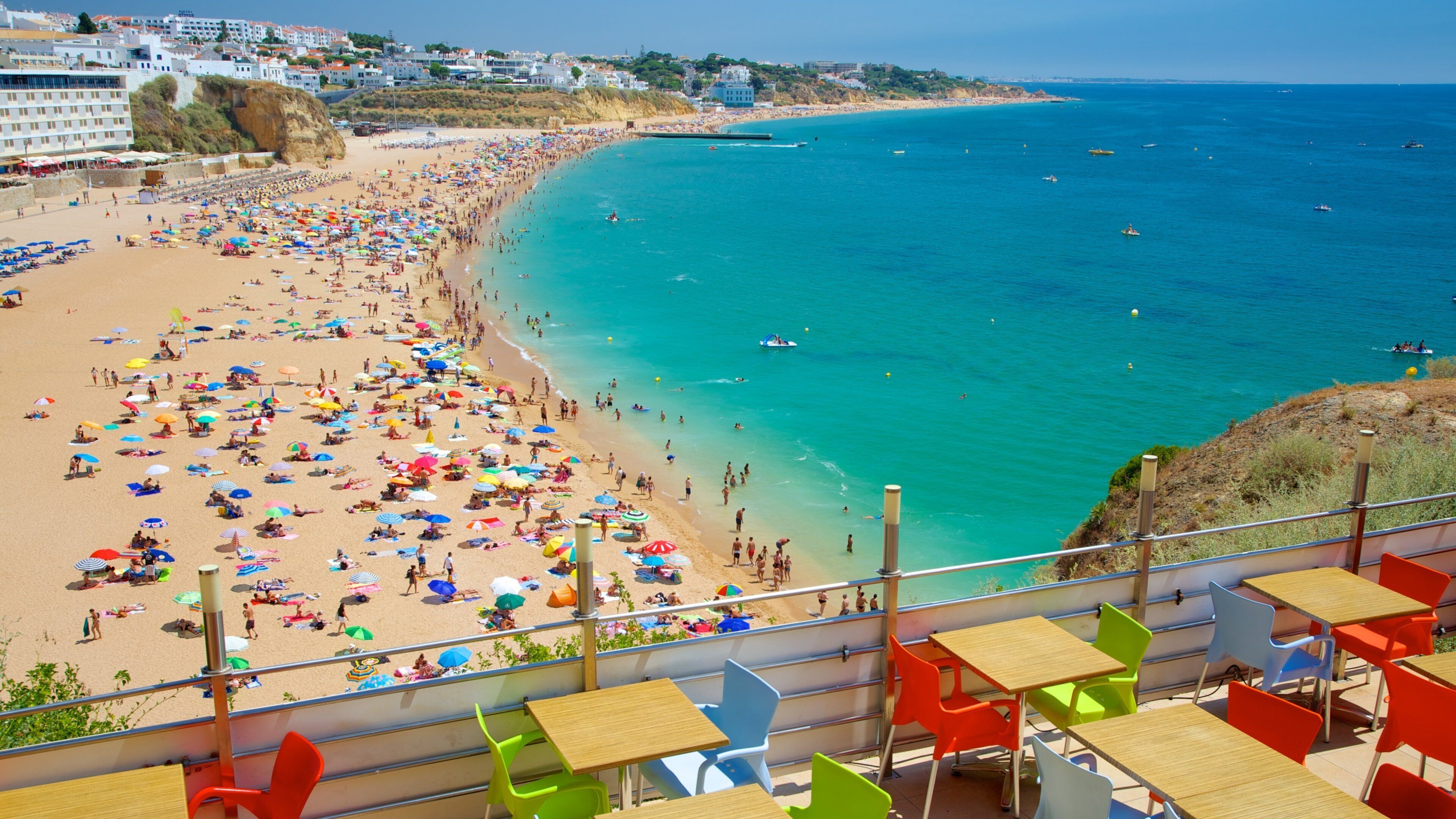 A crowded beach with colorful umbrellas and people enjoying the water.