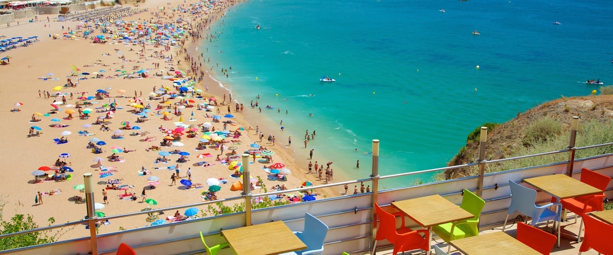 A crowded beach with colorful umbrellas and people enjoying the water.