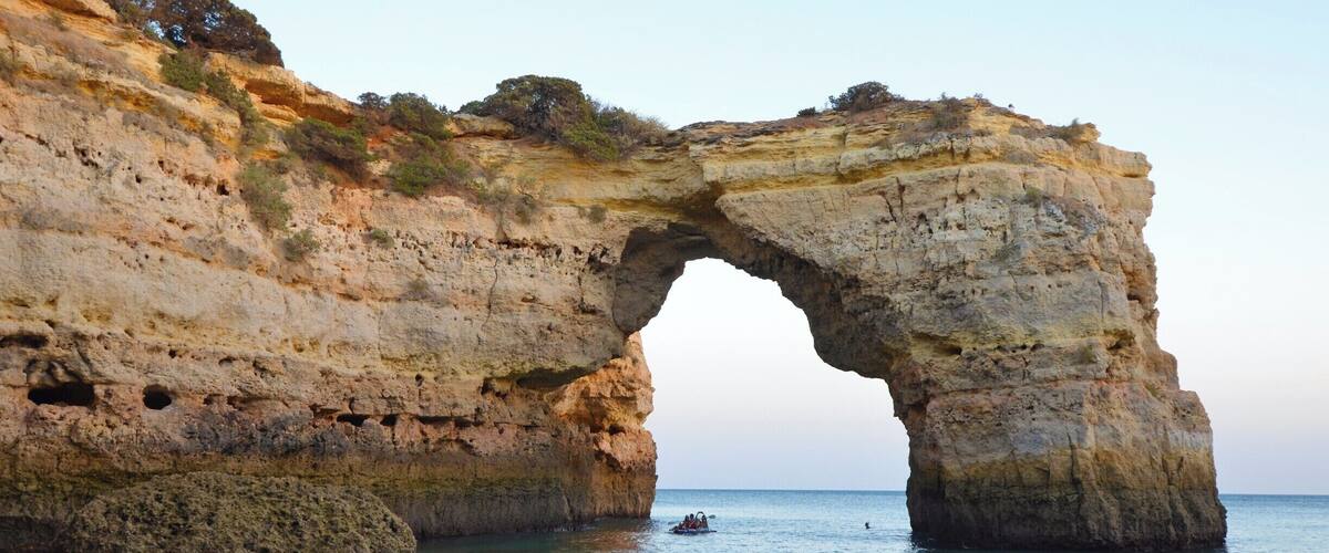 A natural rock arch formation with a boat in the water.