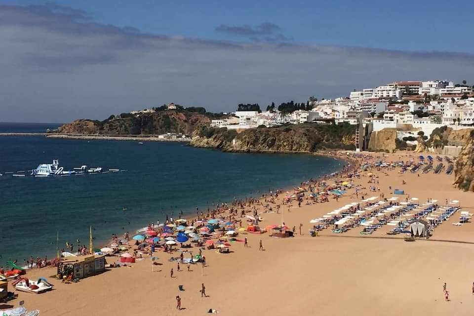 A crowded beach with people, umbrellas, and boats.