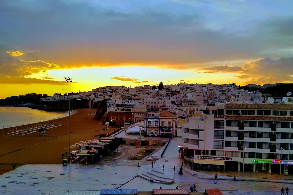 A coastal cityscape at sunset with a beach, buildings, and a clear sky.