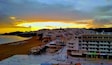 Une vue d’une ville côtière au coucher du soleil, avec une plage, des bâtiments et un ciel dégagé.