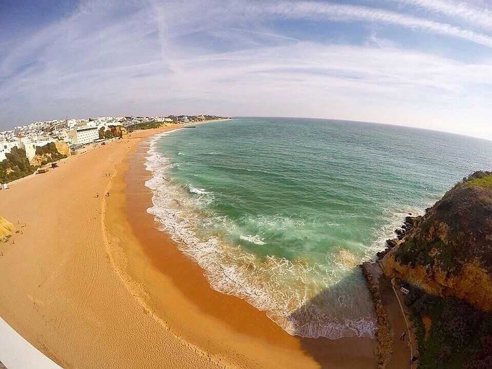 A coastal beach with clear turquoise waters, sandy shore, and buildings along the coastline.