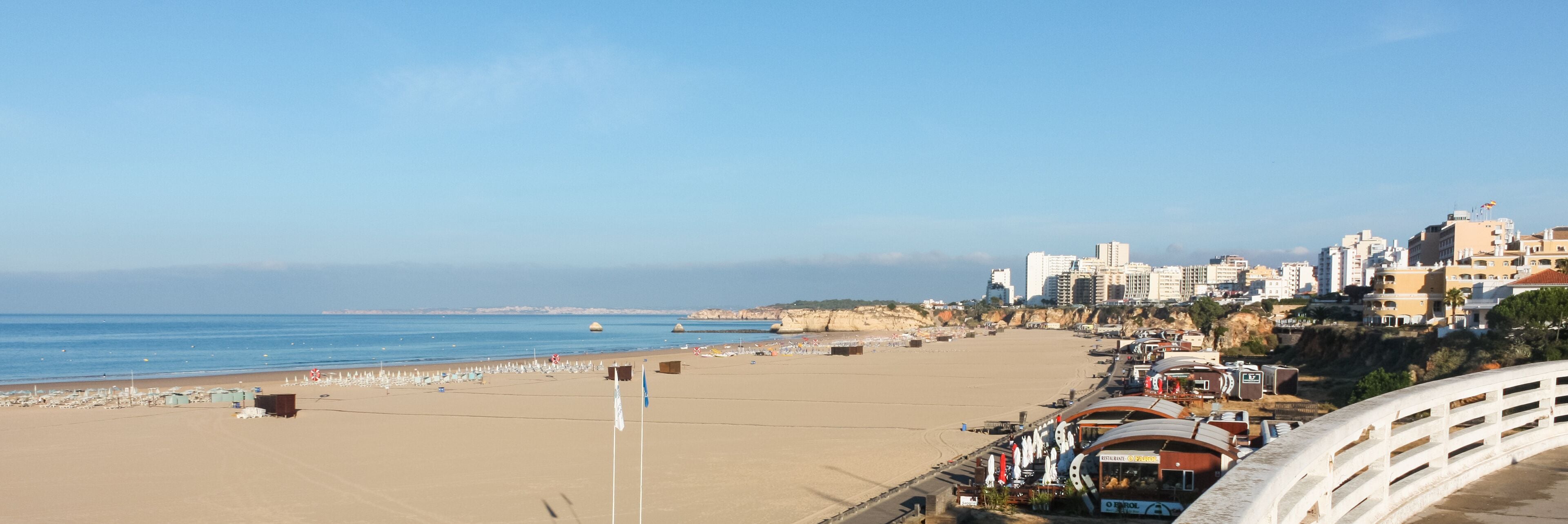 Una playa con cielo despejado, orilla arenosa y edificios al fondo.