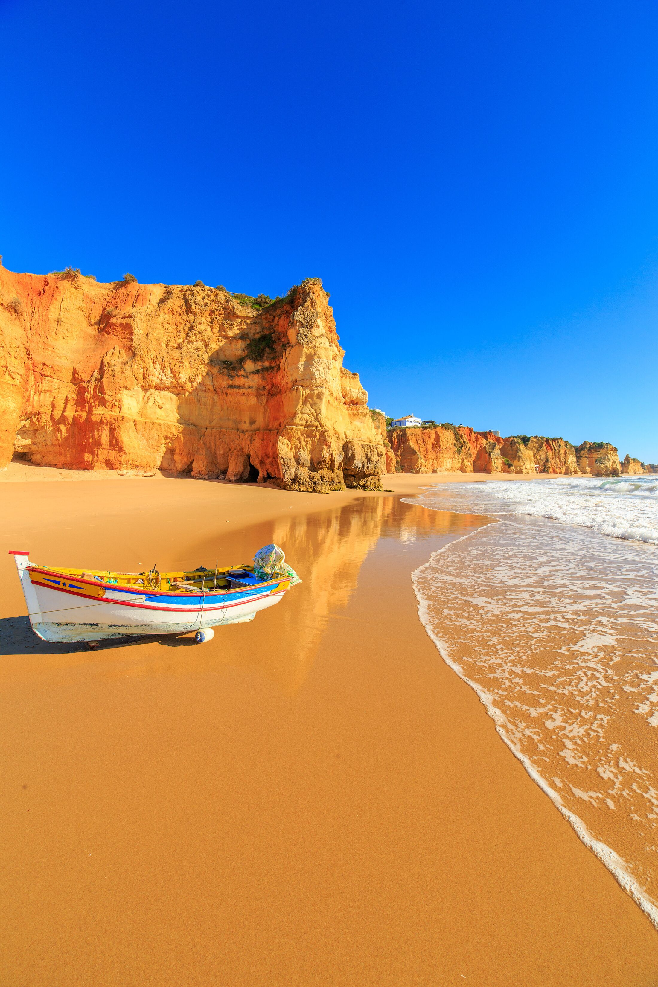 A boat on a sandy beach with cliffs in the background.