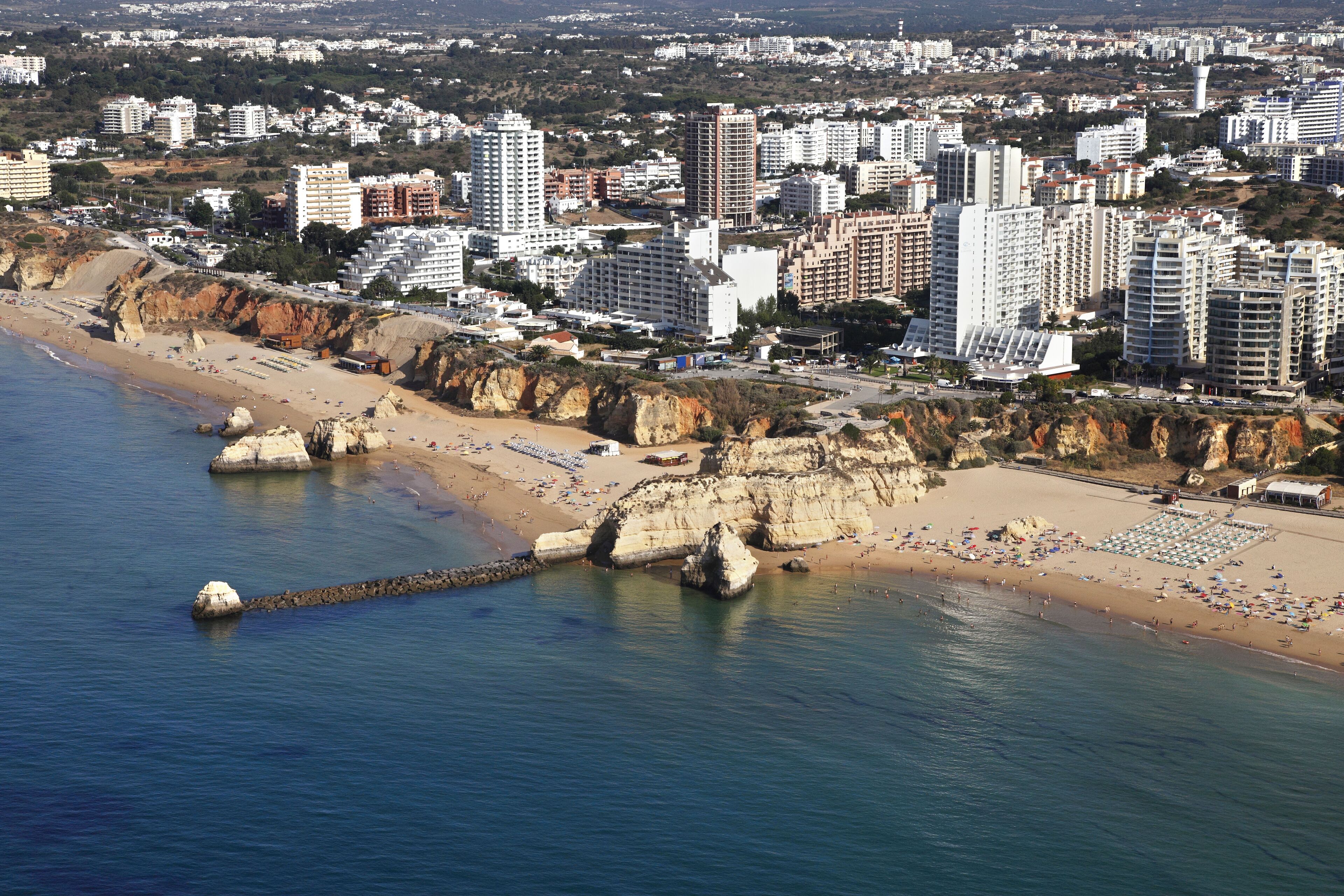 A coastal cityscape with a sandy beach, rocky cliffs, and numerous high-rise buildings.