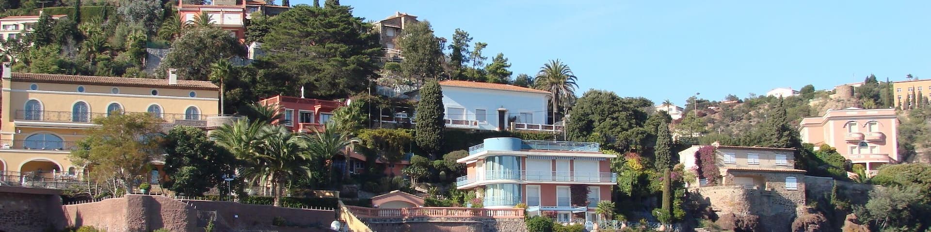 A coastal town with buildings on a hillside, a bridge, and a rocky shoreline.