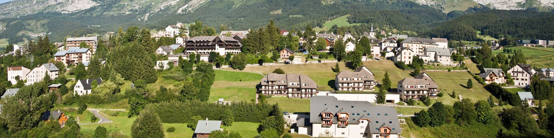 A mountainous village with houses and buildings nestled among green hills and rocky peaks.