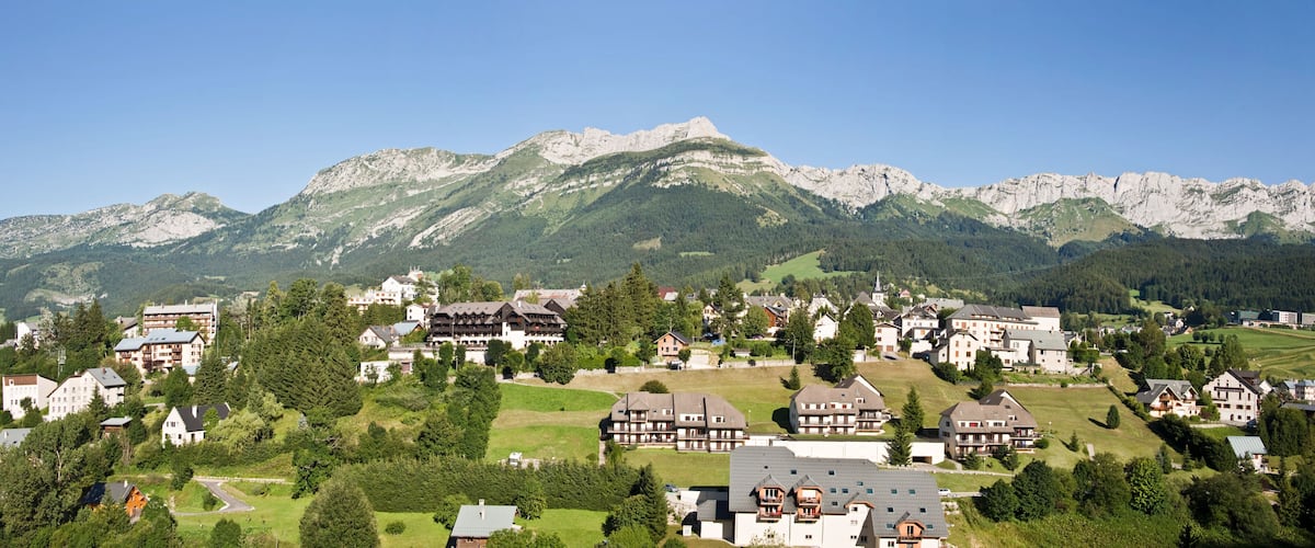 A mountainous village with houses and buildings nestled among green hills and rocky peaks.