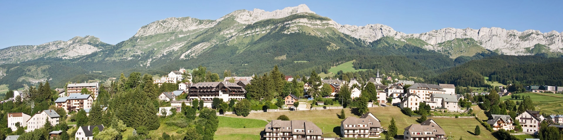 A mountainous village with houses and buildings nestled among green hills and rocky peaks.